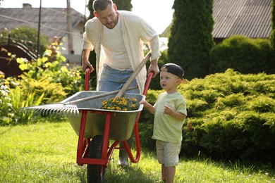 Photo of Father with his son holding wheelbarrow full of beautiful flowers and gardening tools outdoors