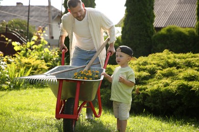 Father with his son holding wheelbarrow full of beautiful flowers and gardening tools outdoors