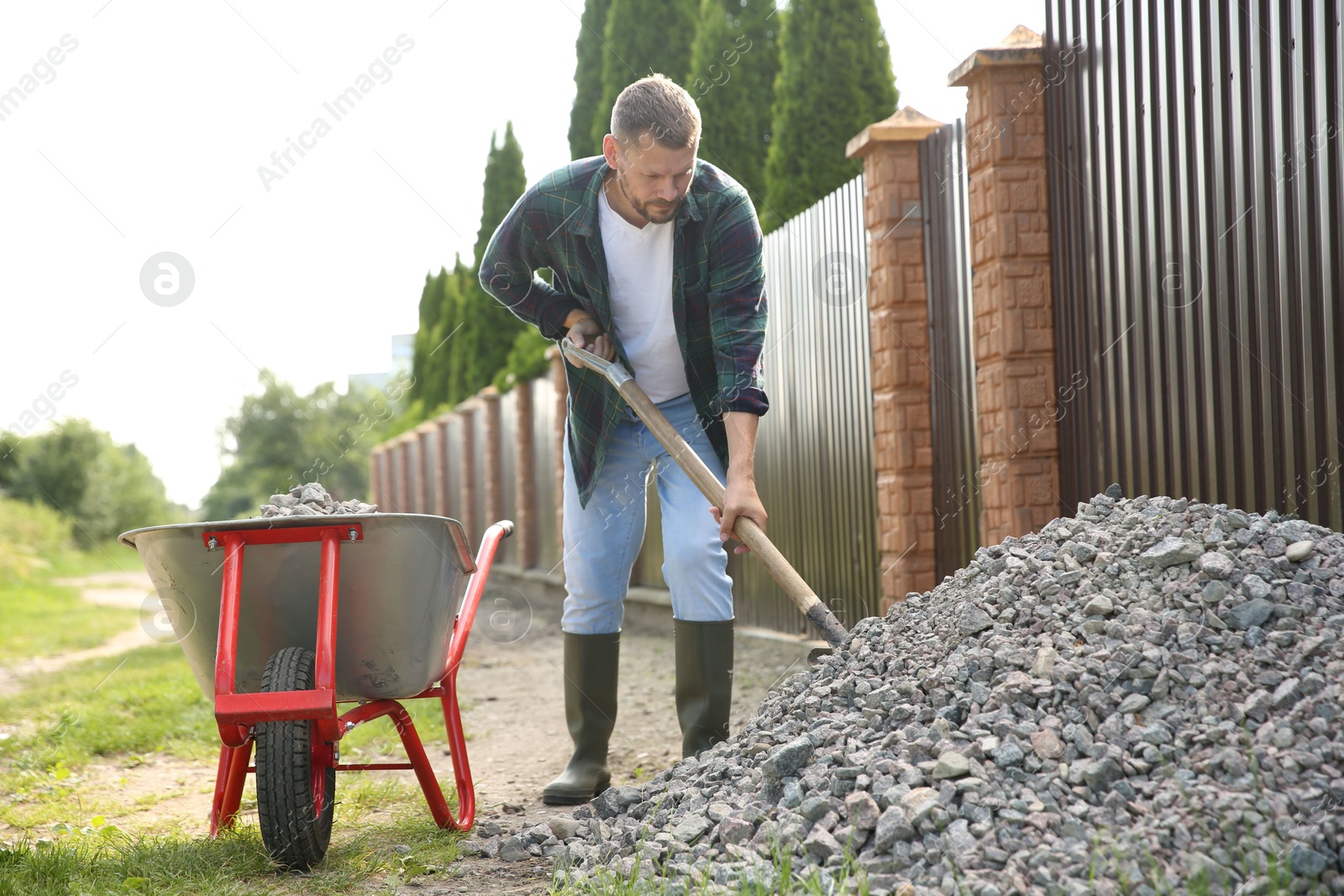 Photo of Man picking stones up with shovel and wheelbarrow outdoors
