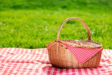 Photo of One picnic wicker basket with checkered napkin and blanket on green grass. Space for text