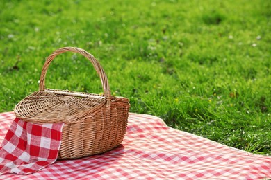 Photo of One picnic wicker basket with checkered napkin and blanket on green grass. Space for text