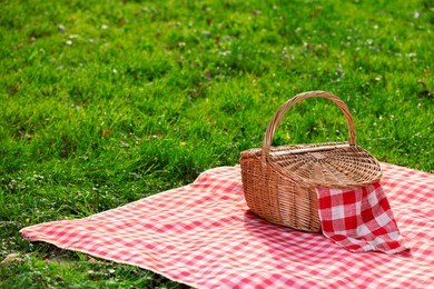 Photo of One picnic wicker basket with checkered napkin and blanket on green grass. Space for text