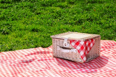 Photo of One picnic wicker basket with checkered napkin and blanket on green grass. Space for text