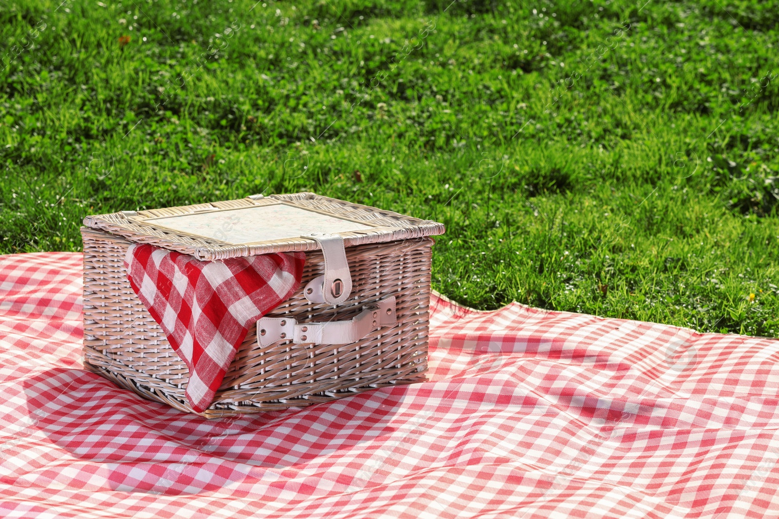 Photo of One picnic wicker basket with checkered napkin and blanket on green grass. Space for text