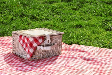 Photo of One picnic wicker basket with checkered napkin and blanket on green grass. Space for text