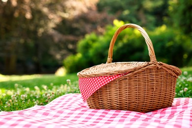 Photo of One picnic wicker basket with checkered napkin and blanket on green grass. Space for text