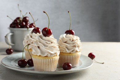 Delicious cupcakes with cream and cherries on light textured table, closeup. Space for text