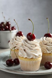 Delicious cupcakes with cream and cherries on light table, closeup