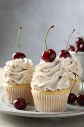 Delicious cupcakes with cream and cherries on light table, closeup