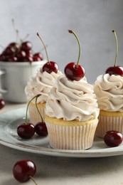 Delicious cupcakes with cream and cherries on light textured table, closeup