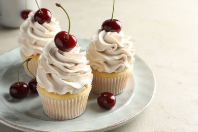 Delicious cupcakes with cream and cherries on light textured table, closeup