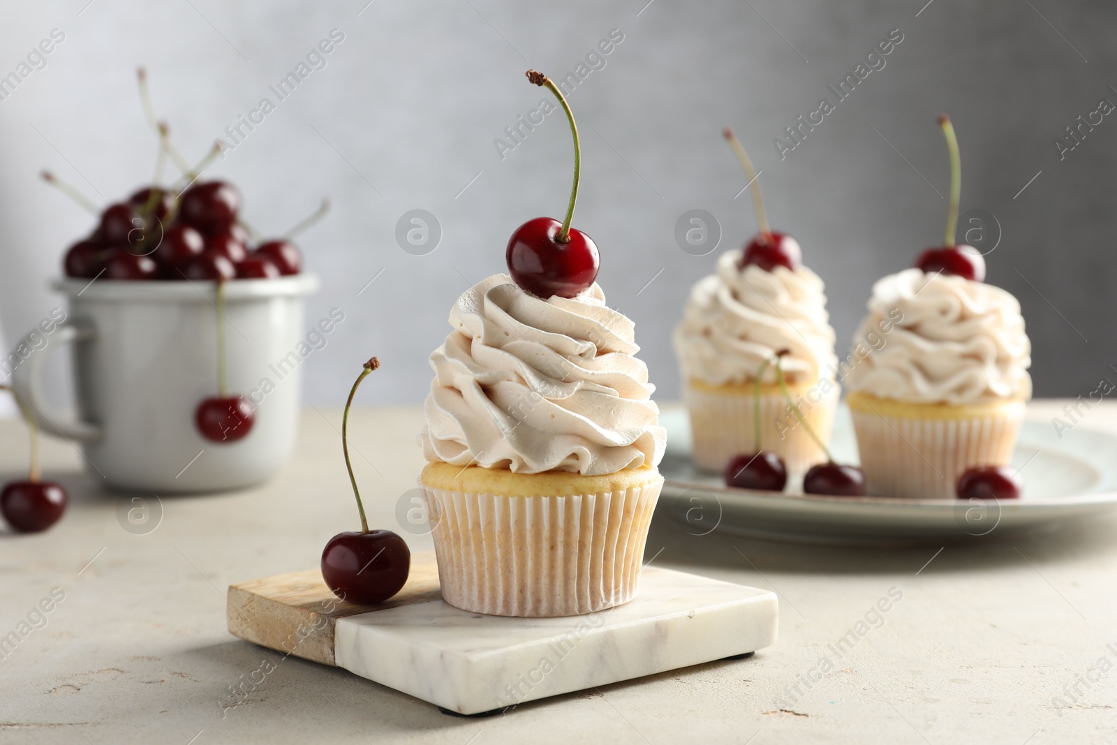 Photo of Delicious cupcakes with cream and cherries on light textured table