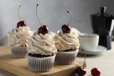 Delicious cupcakes with cream and cherries on light table, closeup