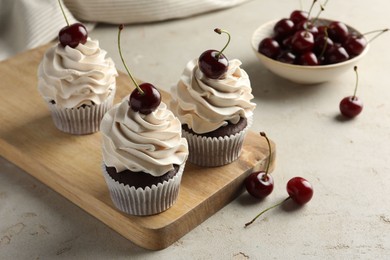 Photo of Delicious cupcakes with cream and cherries on light textured table