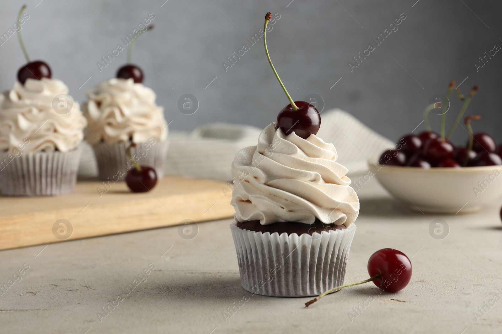 Photo of Delicious cupcakes with cream and cherries on light textured table