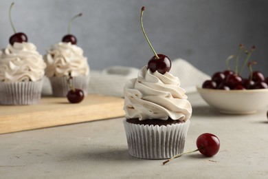 Delicious cupcakes with cream and cherries on light textured table