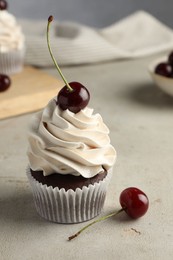 Photo of Delicious cupcake with cream and cherries on light textured table, closeup