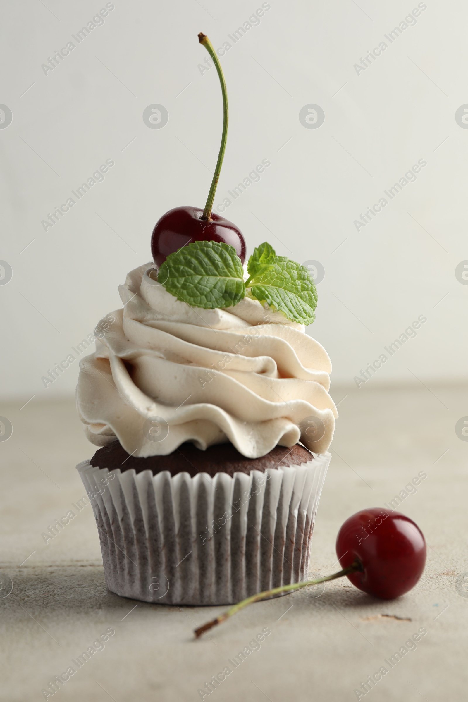 Photo of Delicious cupcake with cherries and fresh mint on light textured table, closeup