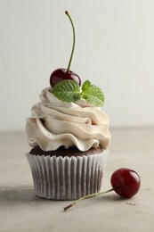 Delicious cupcake with cherries and fresh mint on light textured table, closeup