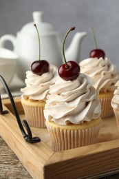 Photo of Delicious cupcakes with cream and cherries on wooden table, closeup