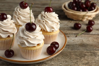 Photo of Delicious cupcakes with cream and cherries on wooden table, closeup