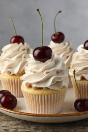 Photo of Delicious cupcakes with cream and cherries on wooden table, closeup