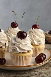 Delicious cupcakes with cream and cherries on wooden table, closeup