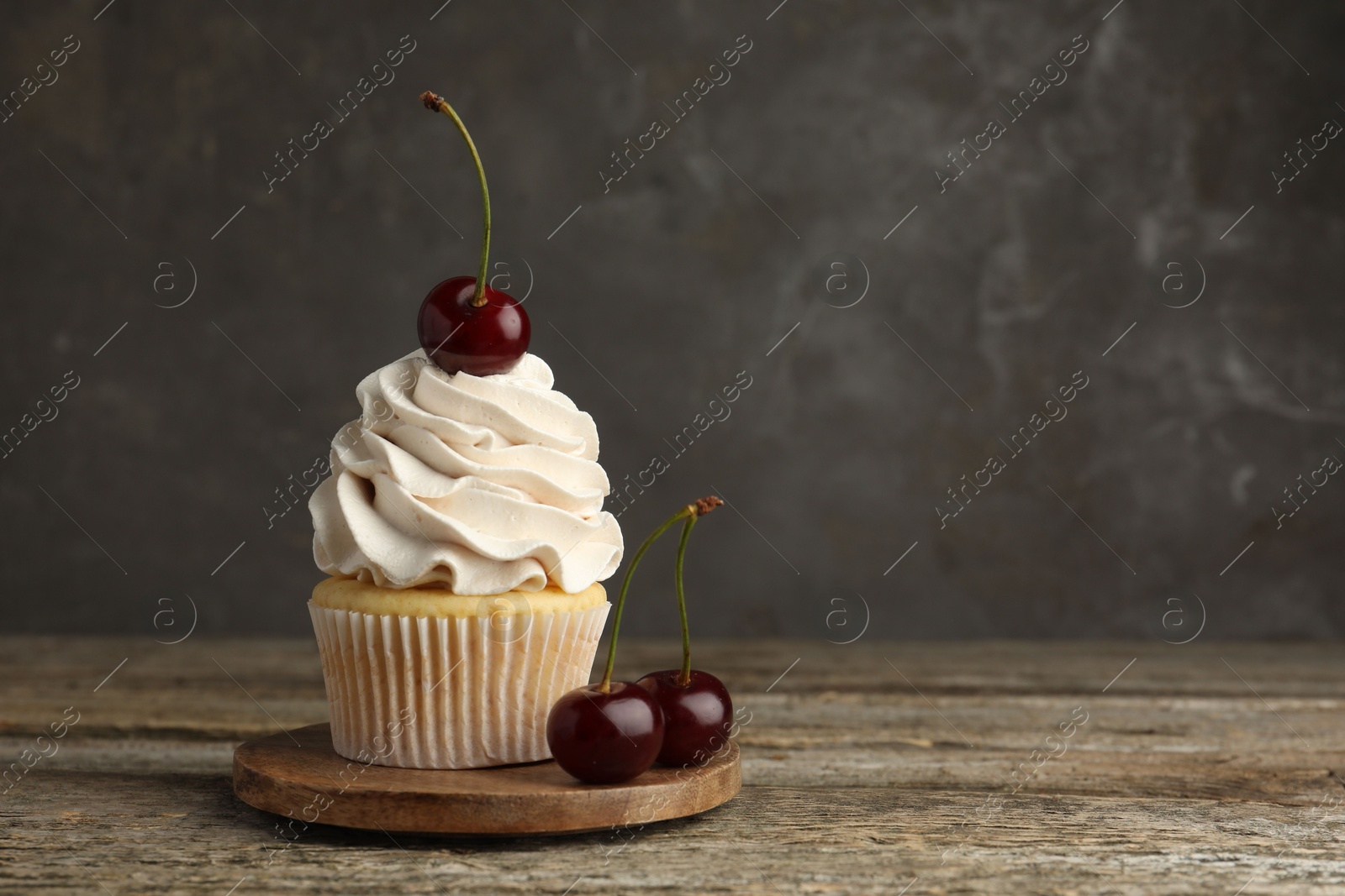 Photo of Delicious cupcake with cream and cherries on wooden table, space for text