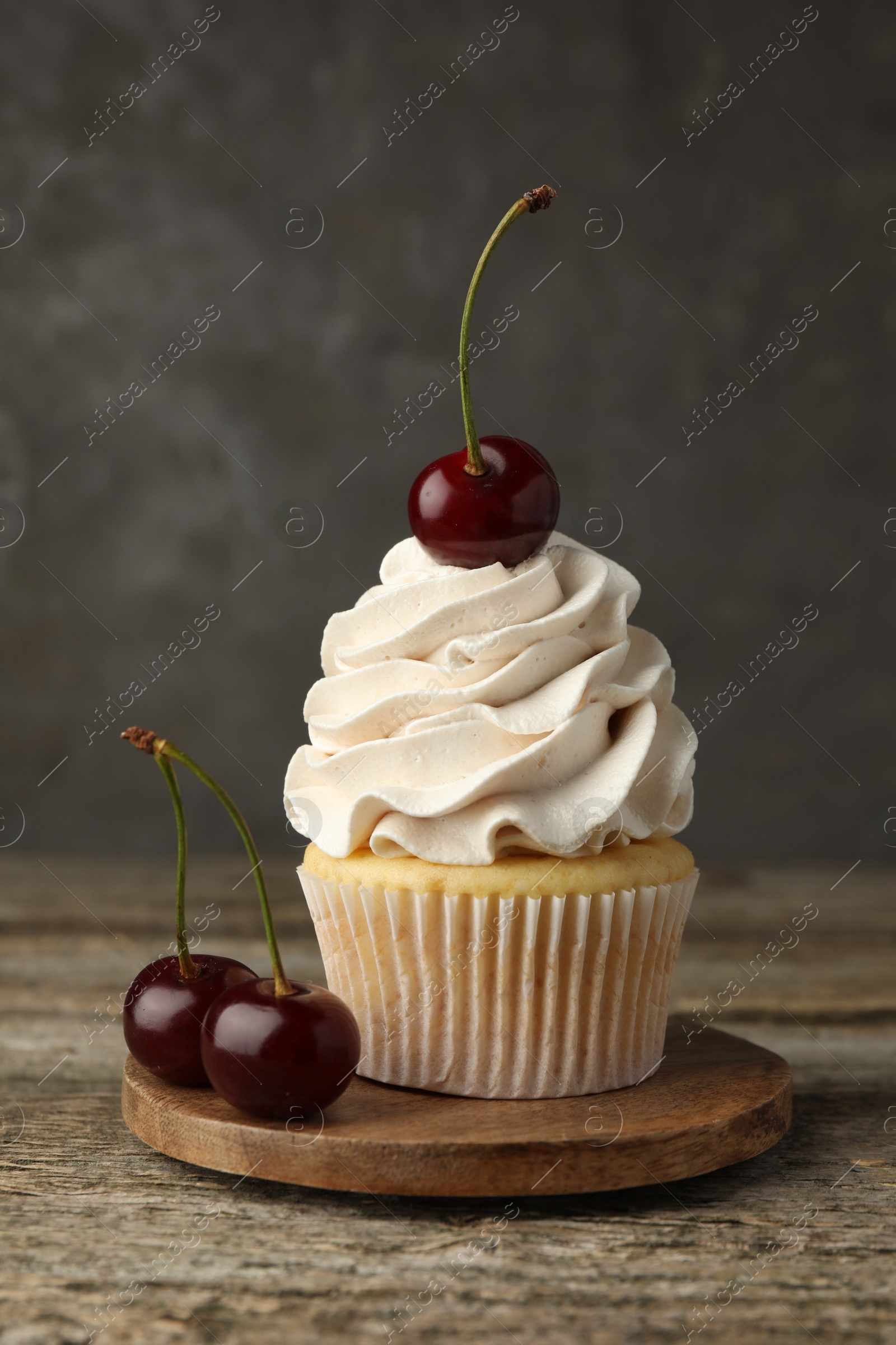 Photo of Delicious cupcake with cream and cherries on wooden table, closeup