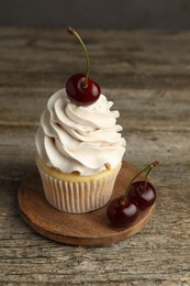 Photo of Delicious cupcake with cream and cherries on wooden table, closeup