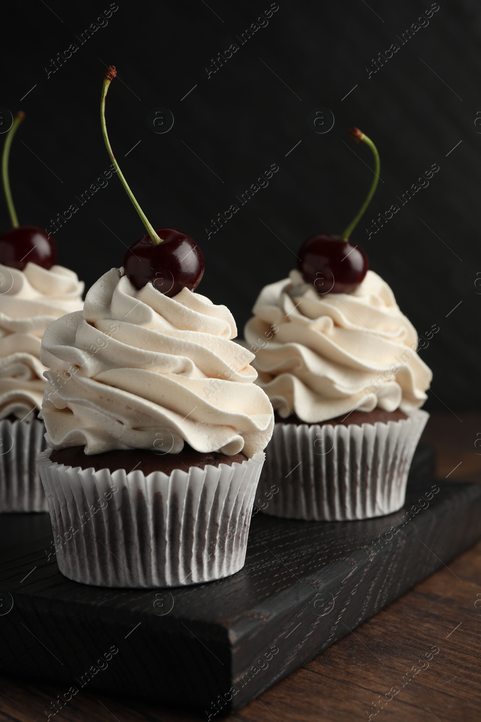 Photo of Delicious cupcakes with cream and cherries on wooden table, closeup