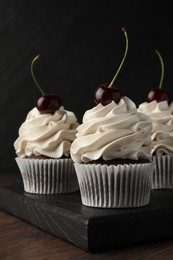 Delicious cupcakes with cream and cherries on wooden table, closeup