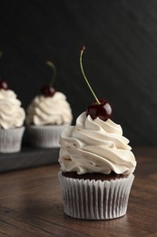 Photo of Delicious cupcakes with cream and cherries on wooden table