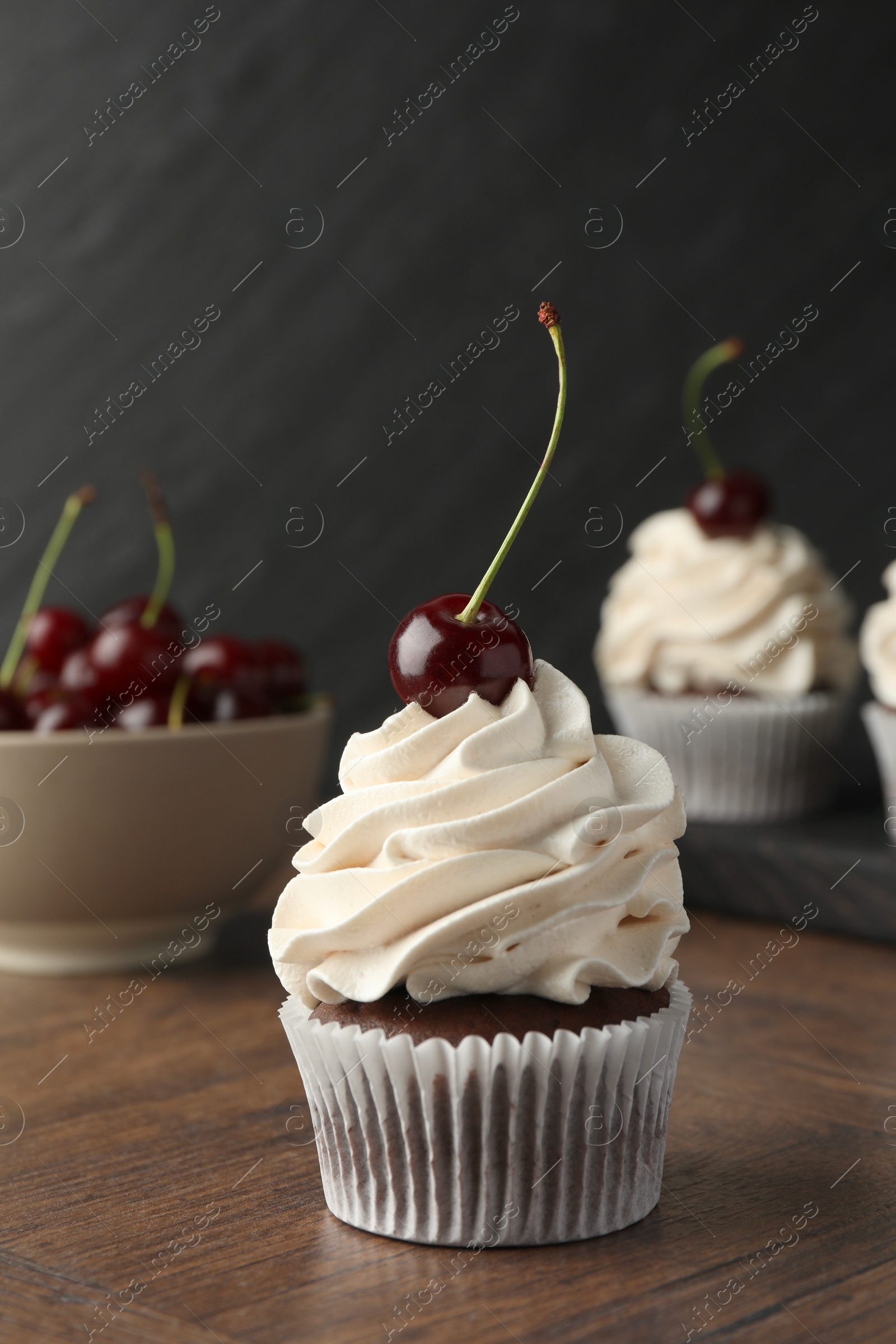 Photo of Delicious cupcakes with cream and cherries on wooden table