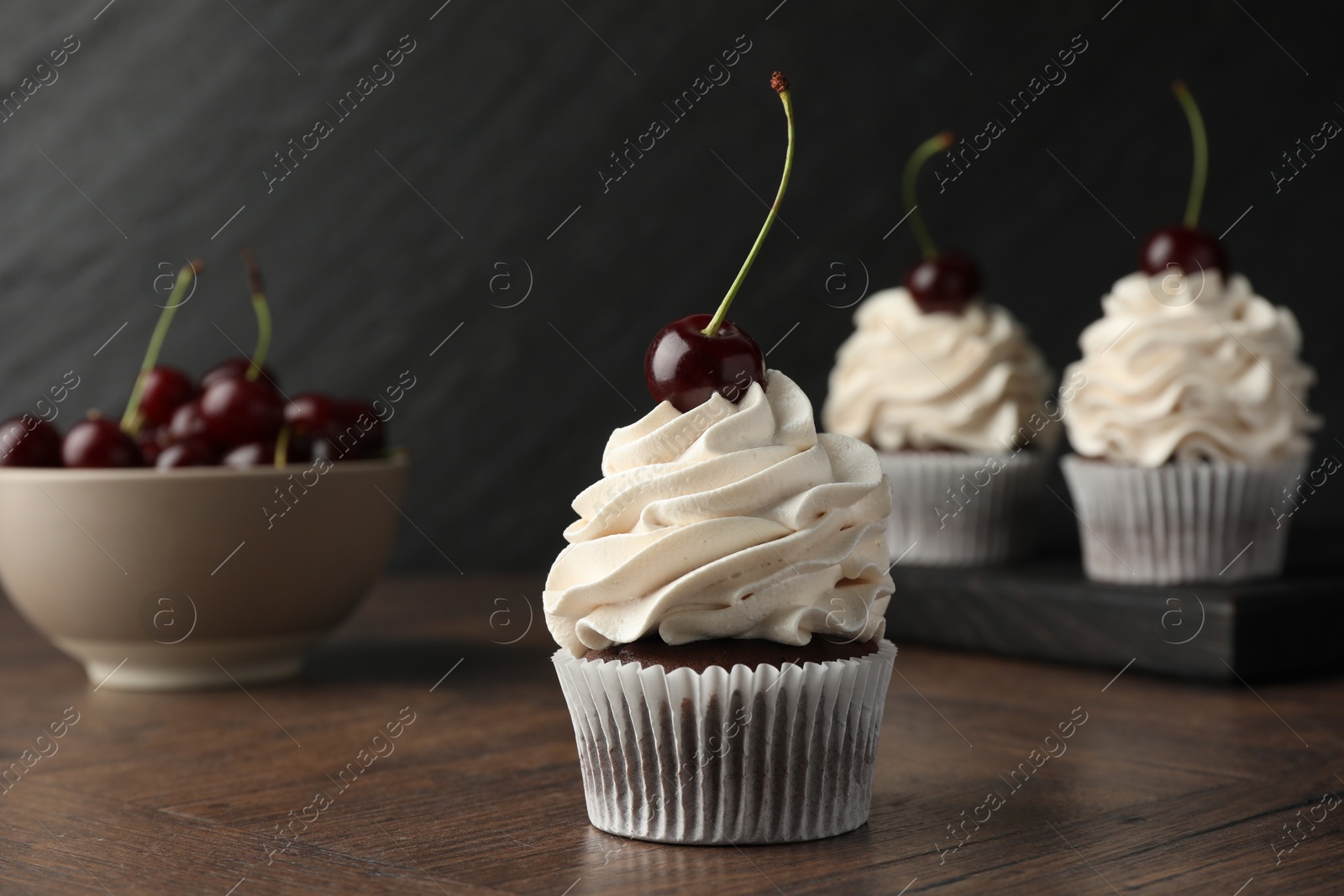 Photo of Delicious cupcakes with cream and cherries on wooden table, closeup