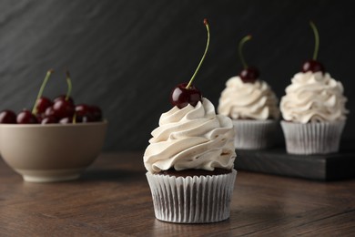 Photo of Delicious cupcakes with cream and cherries on wooden table, closeup