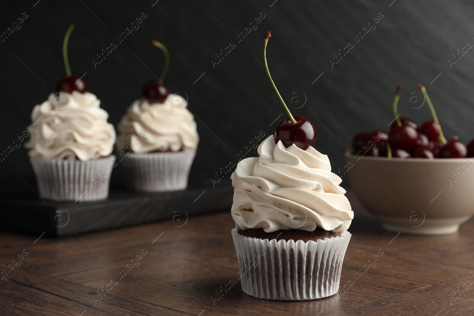 Photo of Delicious cupcakes with cream and cherries on wooden table, closeup