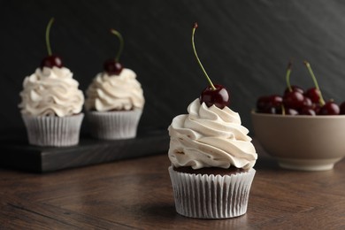 Delicious cupcakes with cream and cherries on wooden table, closeup