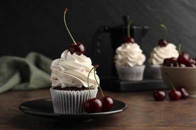 Delicious cupcakes with cream and cherries on wooden table, closeup