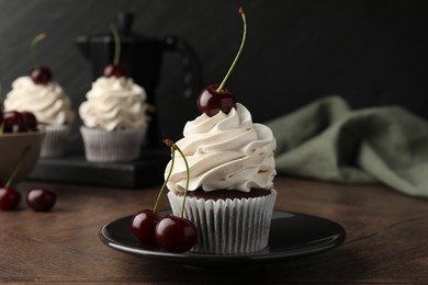 Photo of Delicious cupcakes with cream and cherries on wooden table, closeup