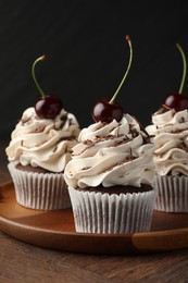 Photo of Delicious cupcakes with cream and cherries on wooden table, closeup