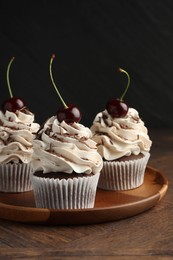 Delicious cupcakes with cream and cherries on wooden table