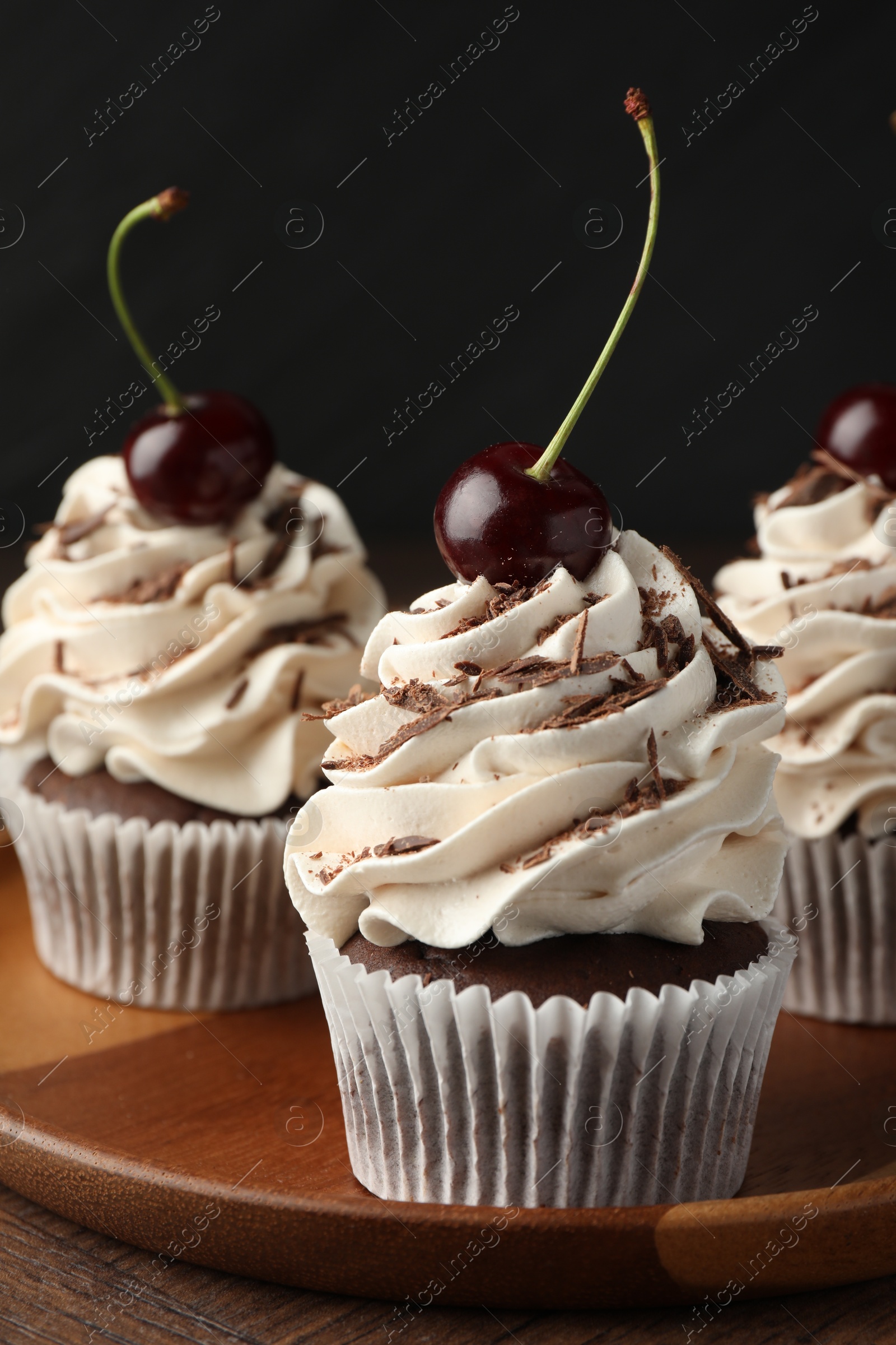 Photo of Delicious cupcakes with cream and cherries on wooden table, closeup