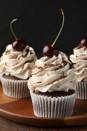 Delicious cupcakes with cream and cherries on wooden table, closeup