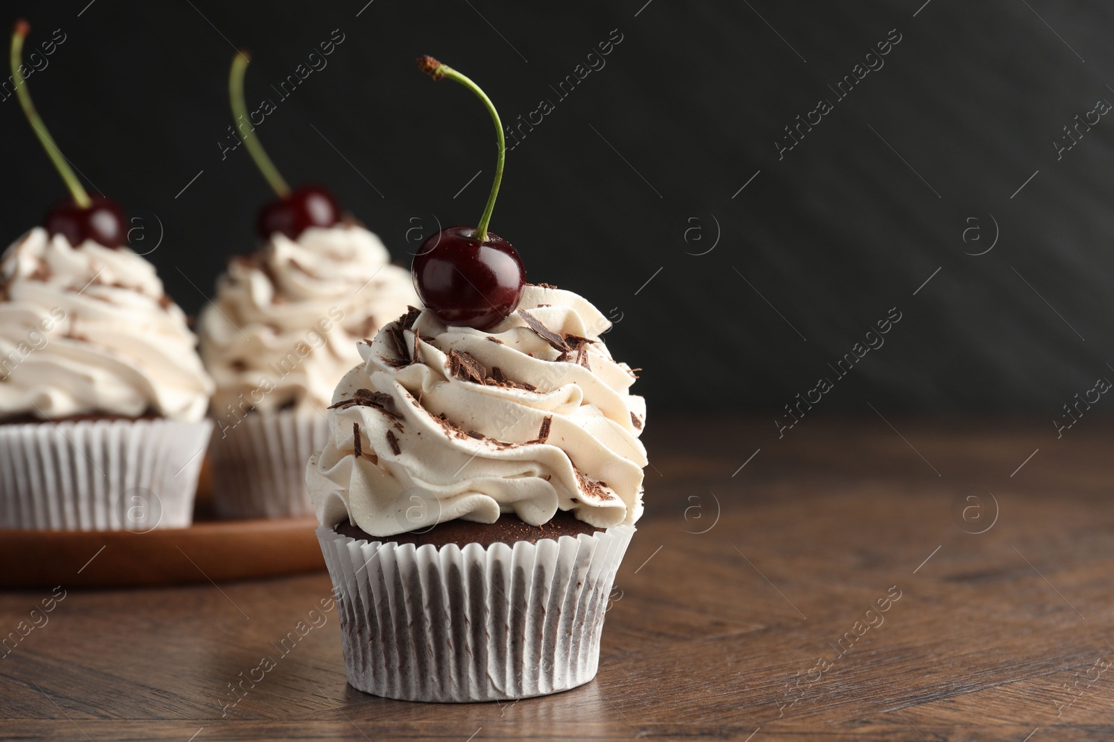 Photo of Delicious cupcakes with cream and cherries on wooden table, closeup. Space for text