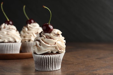 Delicious cupcakes with cream and cherries on wooden table, closeup. Space for text