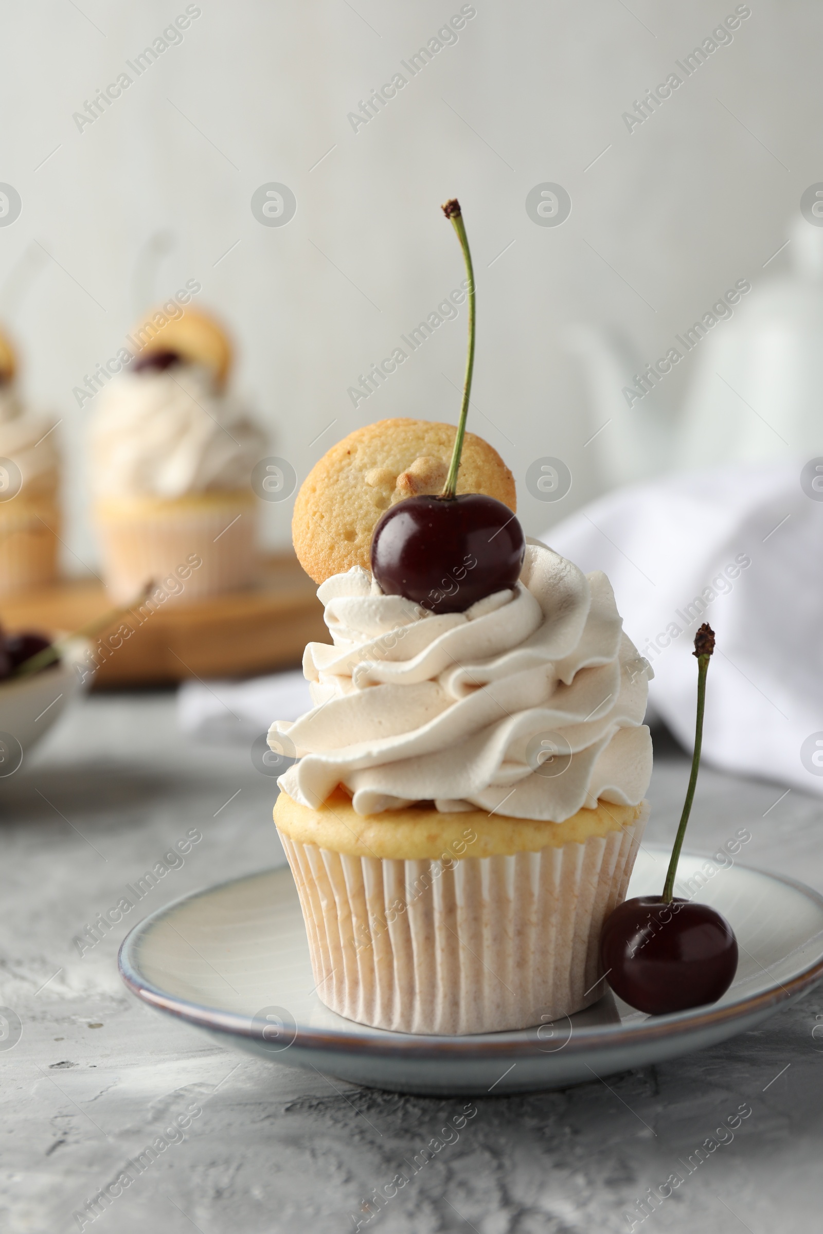 Photo of Delicious cupcake with cherries and cookie on grey textured table, closeup