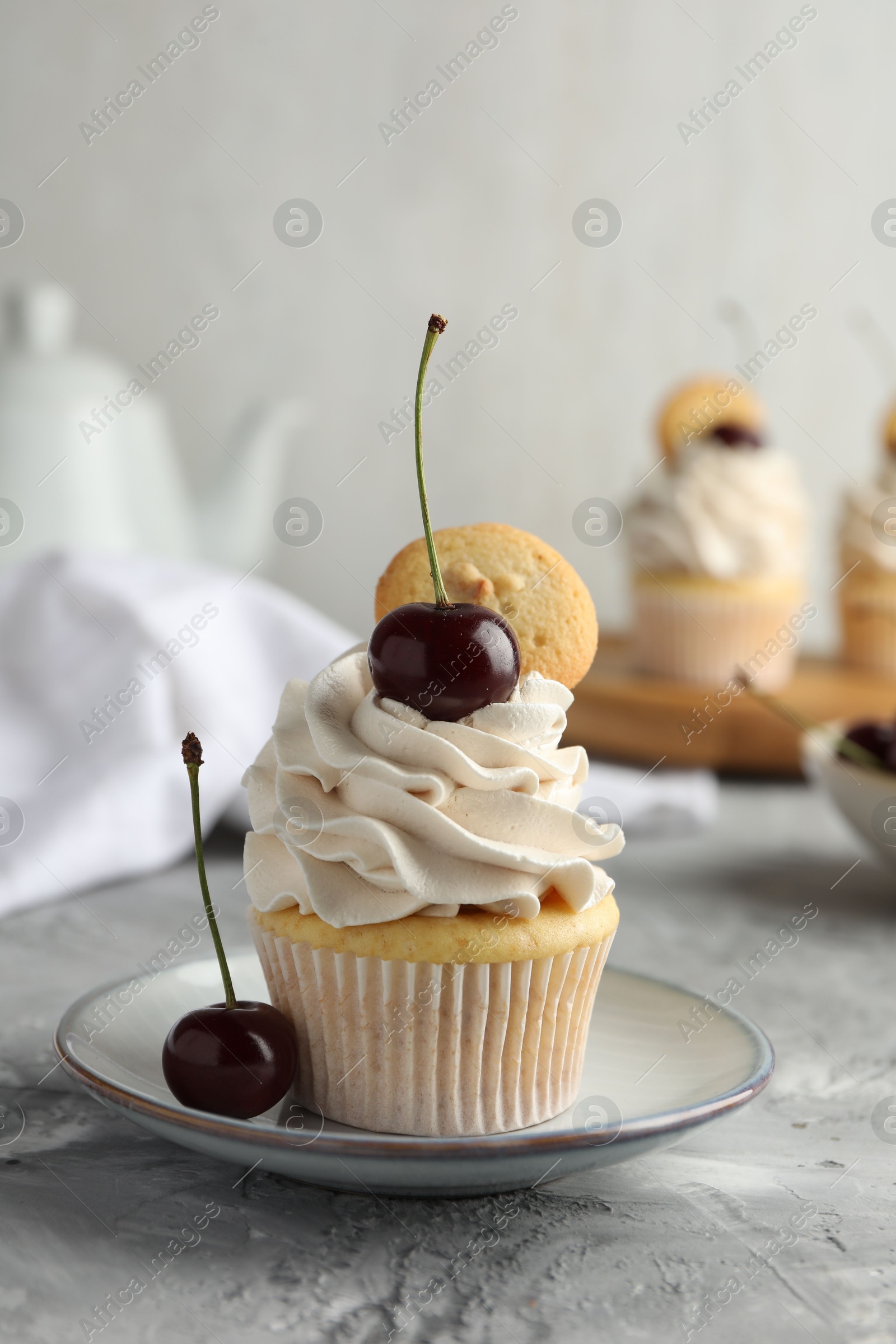 Photo of Delicious cupcake with cherries and cookie on grey textured table