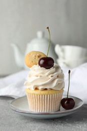 Photo of Delicious cupcake with cherries and cookie on grey textured table, closeup