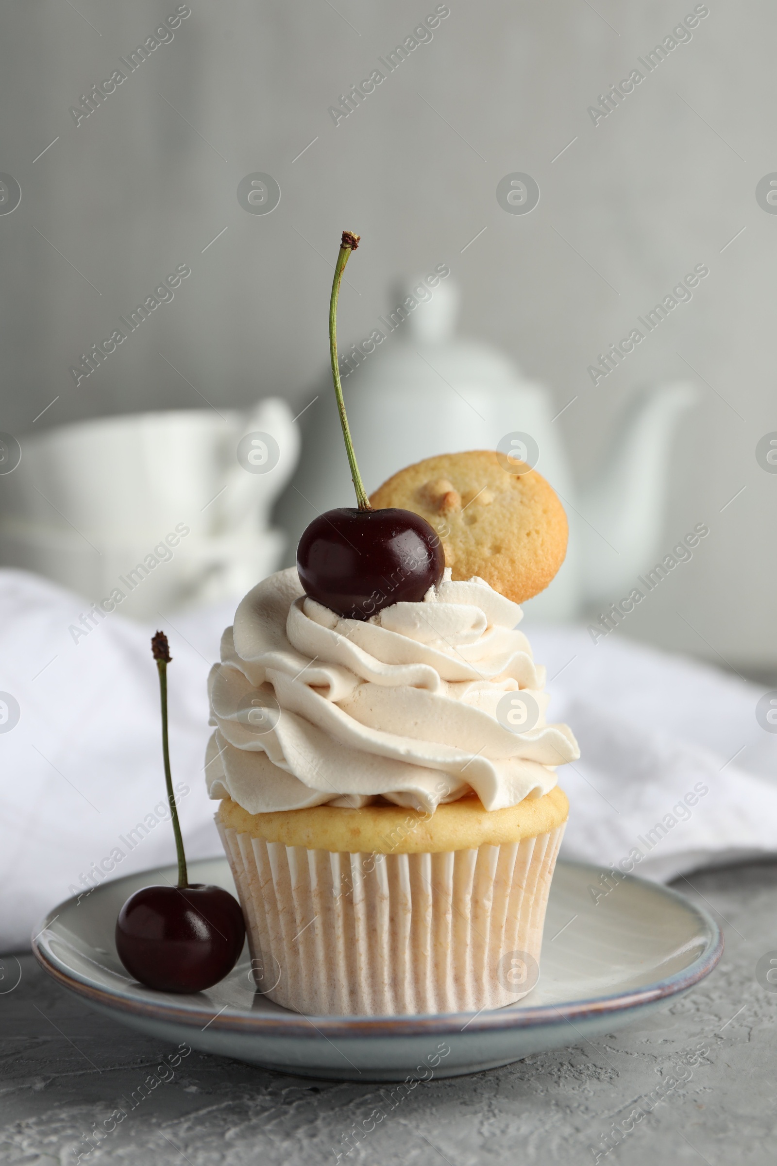 Photo of Delicious cupcake with cherries and cookie on grey textured table, closeup